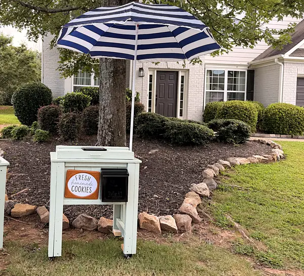 The My Treat stand in a front yard under a blue and white striped umbrella, a hand-lettered Fresh Homemade Cookies sign on the front.